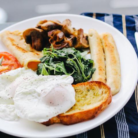 Plate with breakfast food including eggs, spinich, tomatoes, sausage, toast