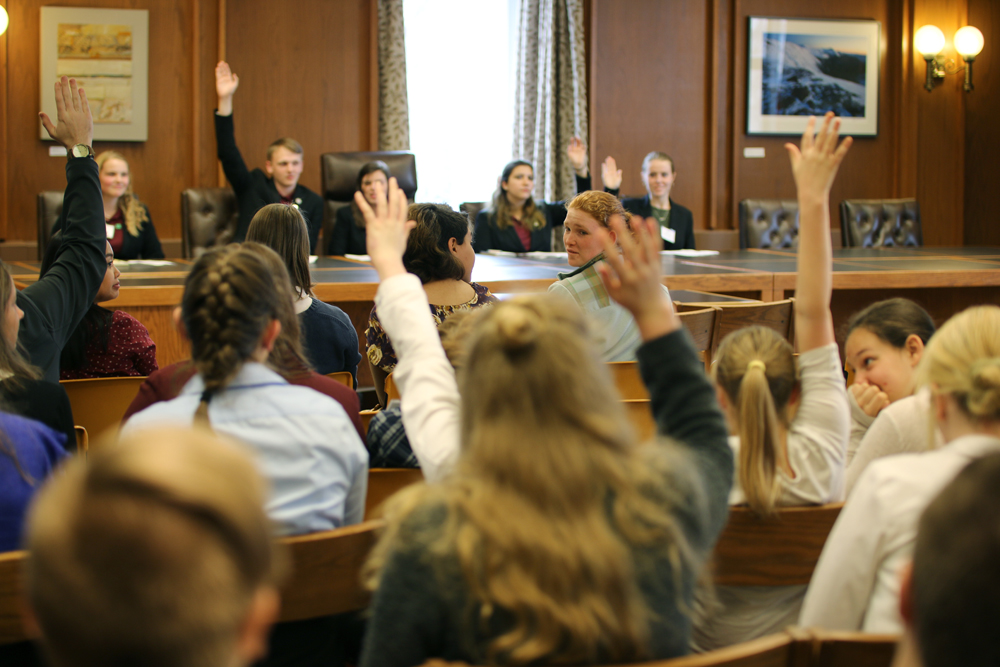 4-H youth are in a meeting room. They are raising their hands as part of a mock legislative vote.
