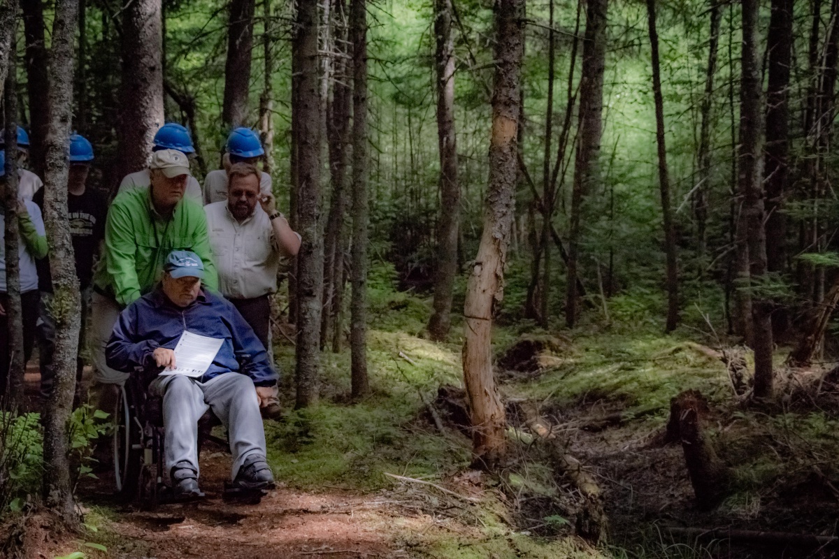 image of a man in a wheelchair accompanied by several people on a forest trail