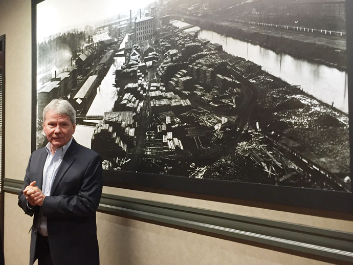 John Clayton stands in front of a picture of the Manchester mills from the 19th century.