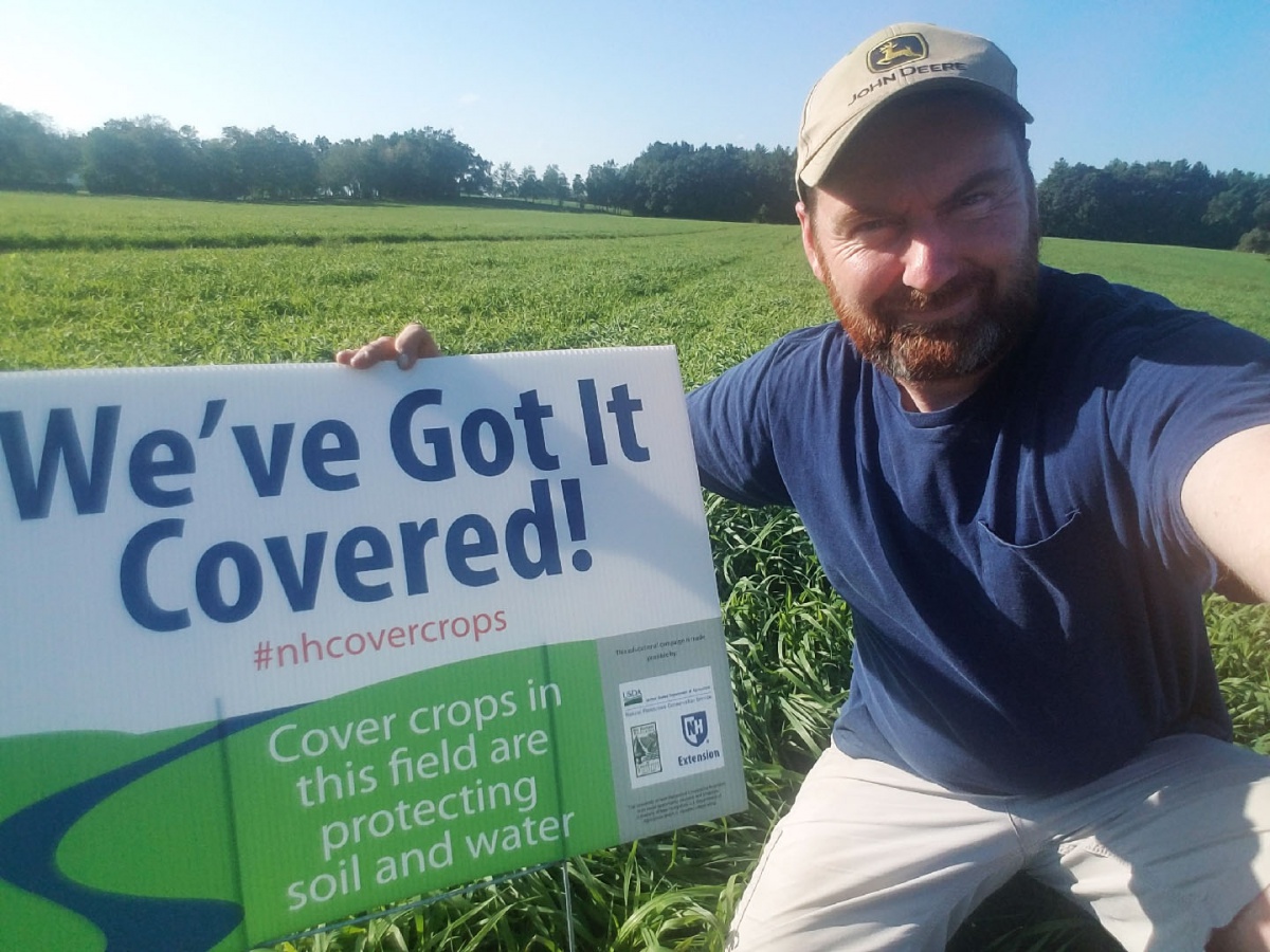 Aiden Lavoie of Hollis poses in a field of winter rye with a We've Got It Covered sign