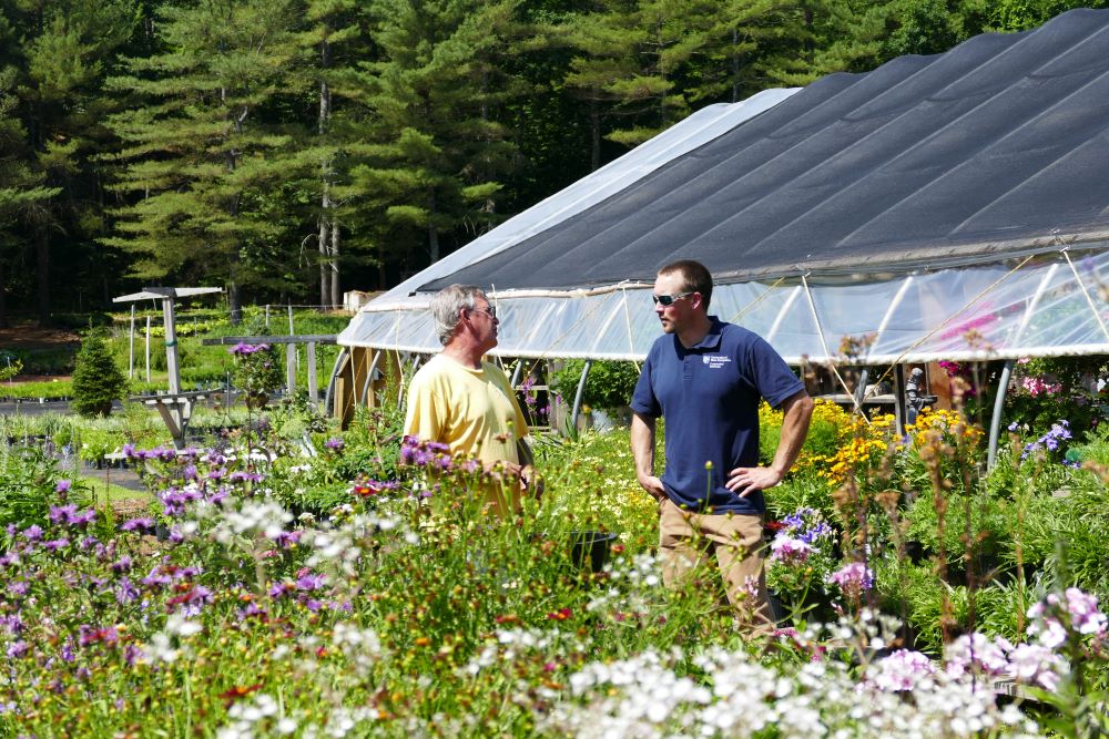 Merrimack County staff talking with resident in field in front of greenhouse