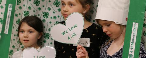 Three children holding a sign "We Love 4-H"