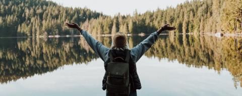 Woman raising arms in front of lake
