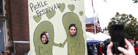 Two people with their faces through holes in a pickle-themed photo opportunity