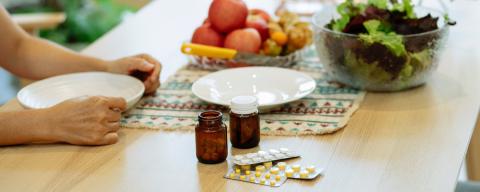 Medication and fresh fruits and veggies placed on table near unrecognizable person.