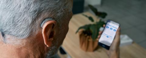 Older man using a mobile device to adjust hearing aid volume.