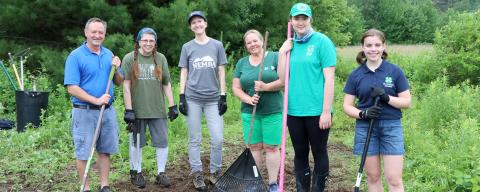 Four adults and two youth standing on a trail, holding rakes