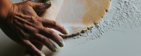 Person's hands rolling flour on dough with rolling pin