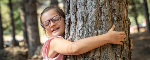 Peaceful little girl with eyes closed finding comfort and serenity hugging a tree.