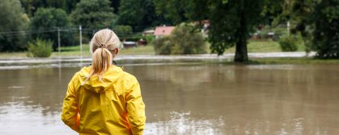 Flooded river. Worried woman looking at overflowing water during flood. Extreme weather and natural disaster due to climate change. by encierro adobe/stock.com