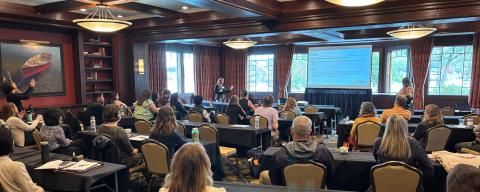 people seated in a large room facing a presenter and presentation screen