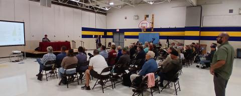 people seated in foldeing chairs in a school gym for a presentation