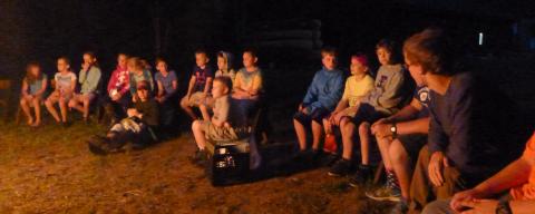 Evening photo of a group of young campers in the glow of a campfire.