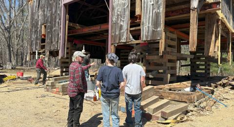 Three people looking at an old barn being lifted