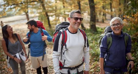 Four people wearing backpacks walking on a trail in the fall