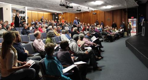 A room of people seated for a community meeting