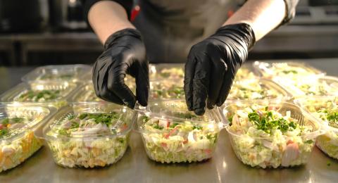 gloved hands packaging salads into plastic to-go containers