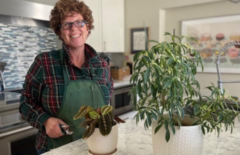 Patti Fried in her kitchen, standing next to two potted plants.
