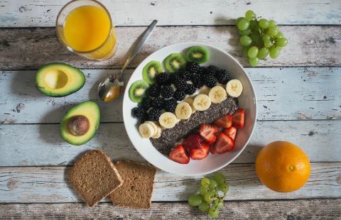 Bowl with fresh fruits, halfed avocado, glass of orange juice, grapes, whole grain bread slices and a whole orange