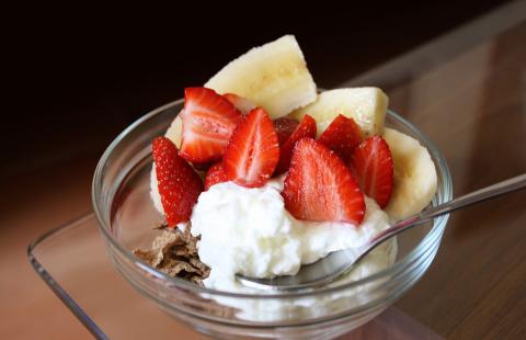 Bowl with dry whole grain cereal, yogurt and sliced strawberries and banana.