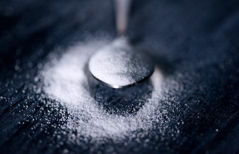 Over flowing spoonful of sugar on a black background.