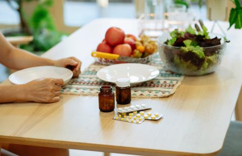 Medication and fresh fruits and veggies placed on table near unrecognizable person.