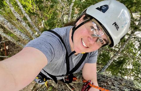 Lindsay Watkins in a tree canopy wearing a helmet and safety glasses