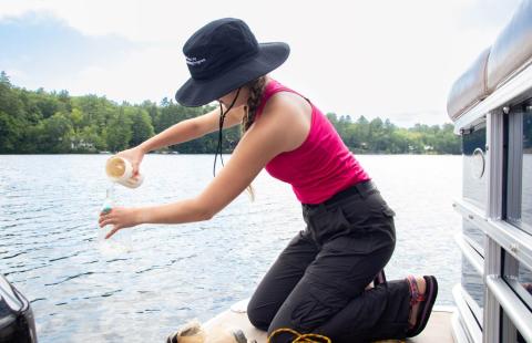 Woman sampling water quality from a boat on a lake in summer