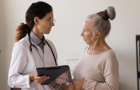 Serious aged woman clinic visitor stand close to confident female doctor with clipboard ask questions about diagnosis. 