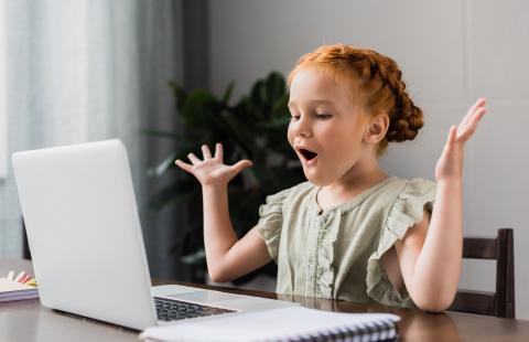 Young red-haired girl at a laptop computer with her hands in the air and an expression of surprise