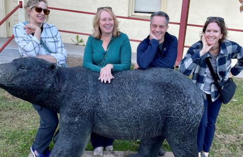 Four people posing behind a statue of a black bear