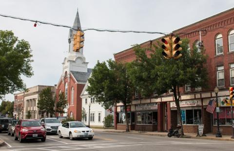 A downtown traffic intersection with tree-lined street, brick commercial buildings and an old brick church.