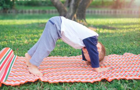 Cute little Asian 1 year old toddler baby boy child practices yoga in Downward Facing Dog Pose and meditating outdoors in nature during the summer time.