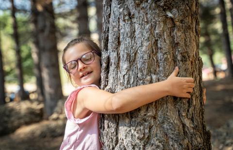 Peaceful little girl with eyes closed finding comfort and serenity hugging a tree.