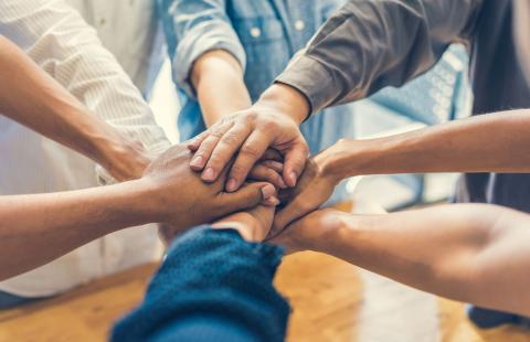 seven people standing in a circle shown from the elbow down with their hands piled in the center