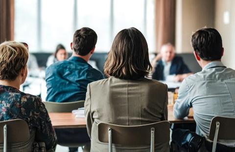 several professionally dressed people sitting at a table facing away