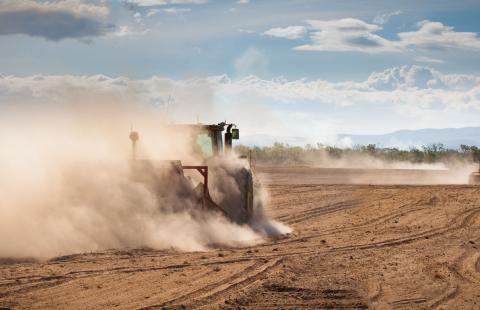 cloud of dust envelop tractor plowing dry field
