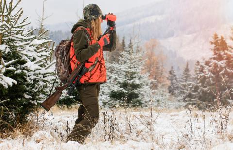 woman in hunting gear using binoculars in wintertime