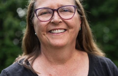 Ann Hamilton wearing purple glasses and dark shirt with trees in the background