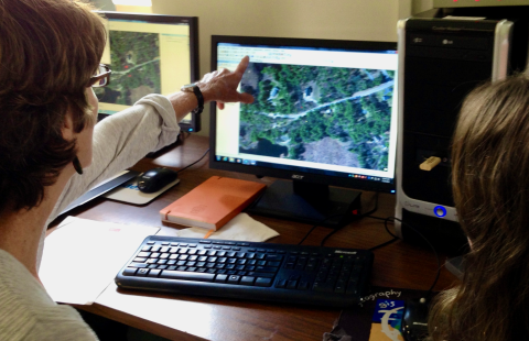 Two people sitting in front of a computer, one of them pointing at a Geographic Information System map on the screen