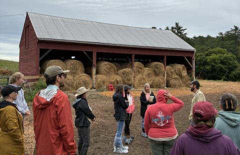 Barn filled with rolls of hay and several farming people surrounding barn