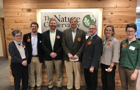 Winners of the The Nature Conservancy's 2017 awards stand in front of the group's sign. There are three women and four men in the photo; all are wearing orange Nature Groupie stickers.