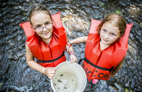 Two girls in river with crawfish in a bucket