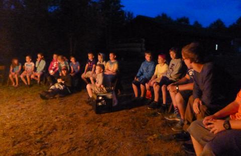 Evening photo of a group of young campers in the glow of a campfire.