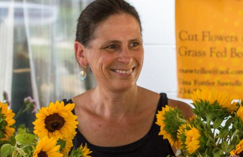 A woman farmer is standing and smiling behind her display of sunflowers