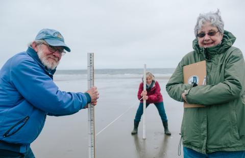 Coastal volunteers hold beach profiling equipment to studying beach geology on a New Hampshire beach.