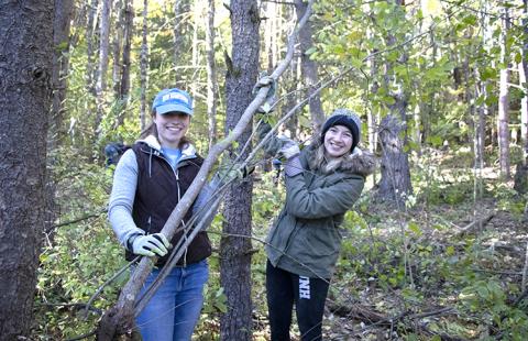 Two UNH students hold a buckthorn shrub they've removed while in college woods for nature groupie