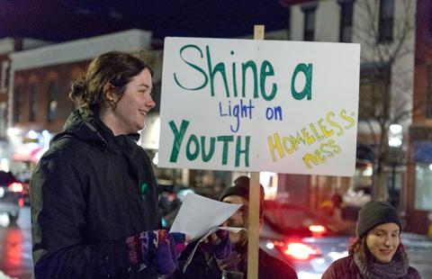 Shine a light on youth homelessness vigil hosted by the Youth on their Own Coalition, attendees hold signs, woman reads from paper to the crowd