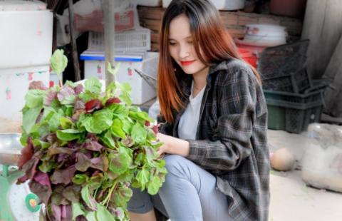 A young woman in a flannel shirt is weighing leafy green vegetables on a scale at a farmers market.